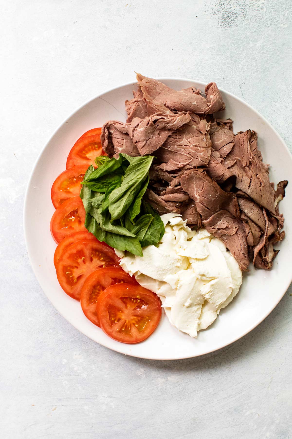 roast beef, tomatoes, basil, and mozzarella on a white plate.