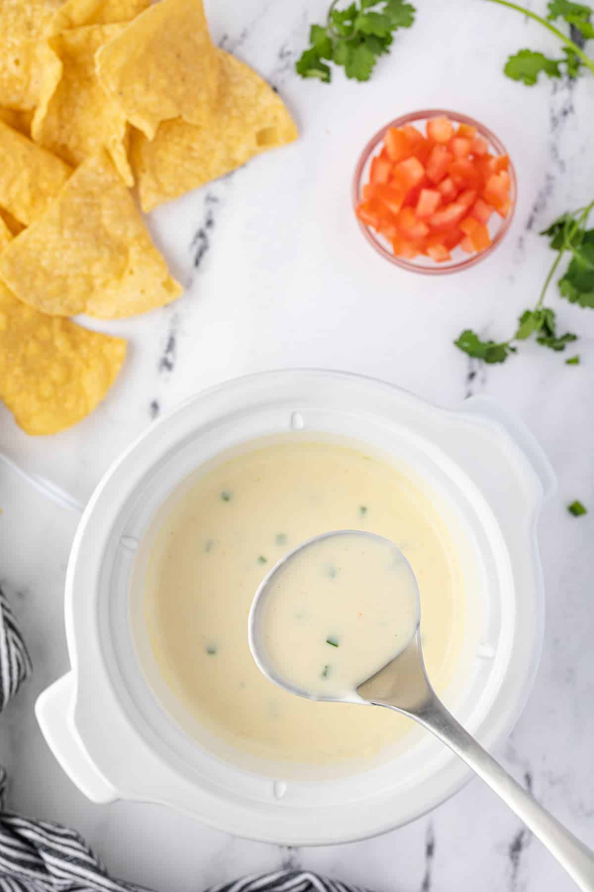 a ladle of queso being lifted out of the slow cooker.