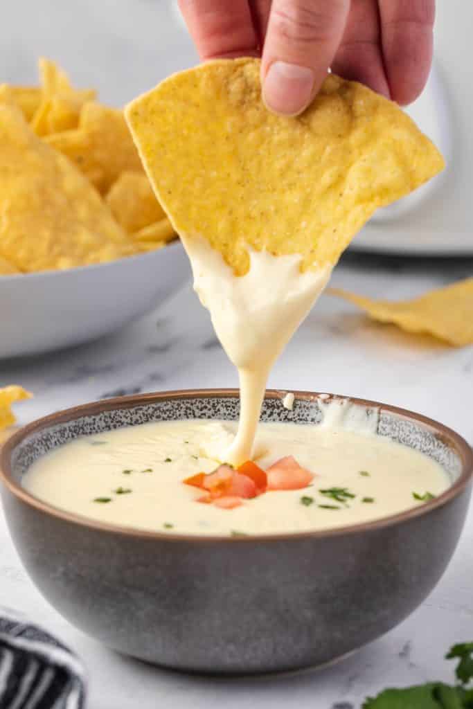 a chip being lifted out of a bowl of queso.