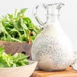 A container of dressing next to a bowl of lettuce.