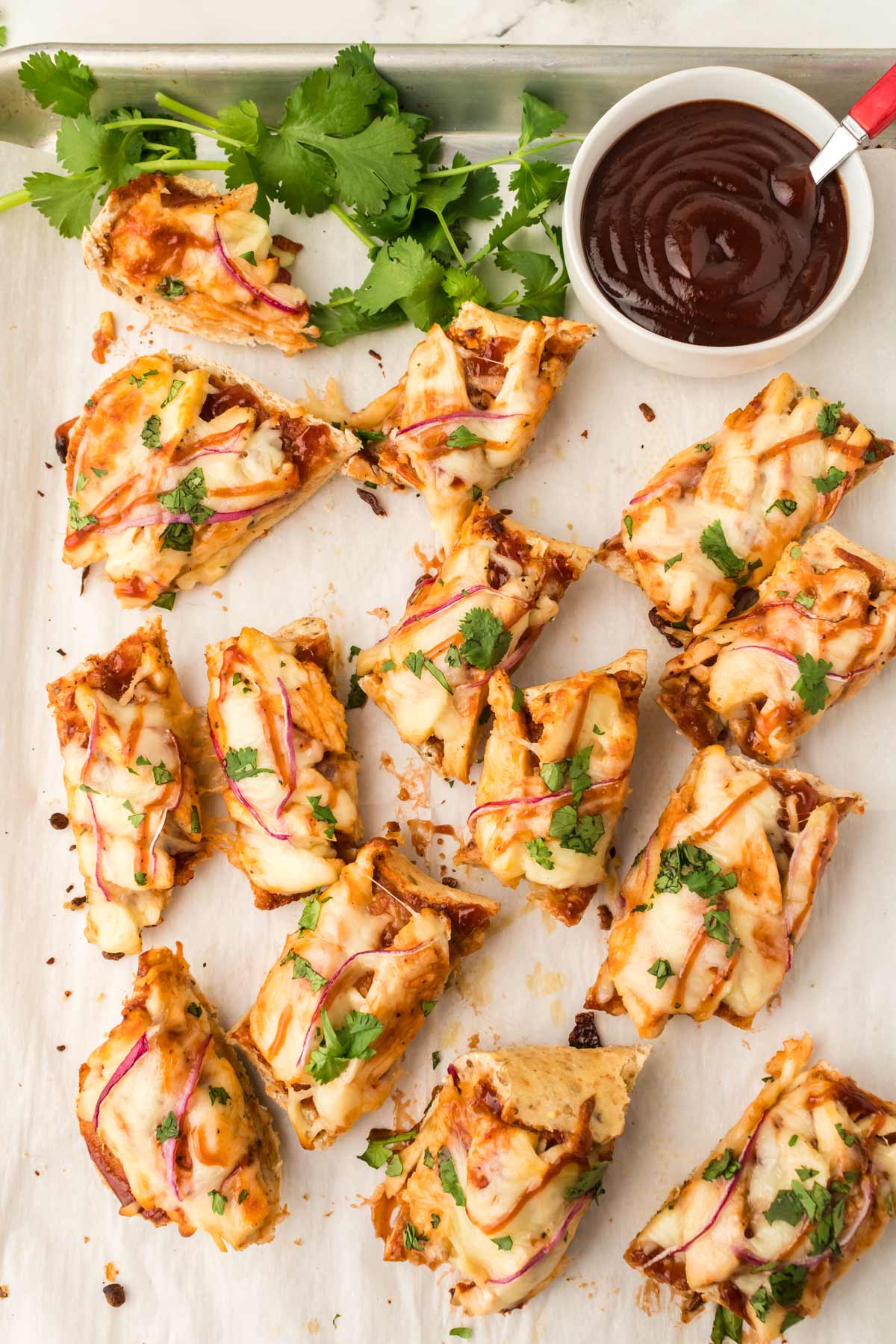 slices of French bread pizza on a pan with a bowl of BBQ sauce.