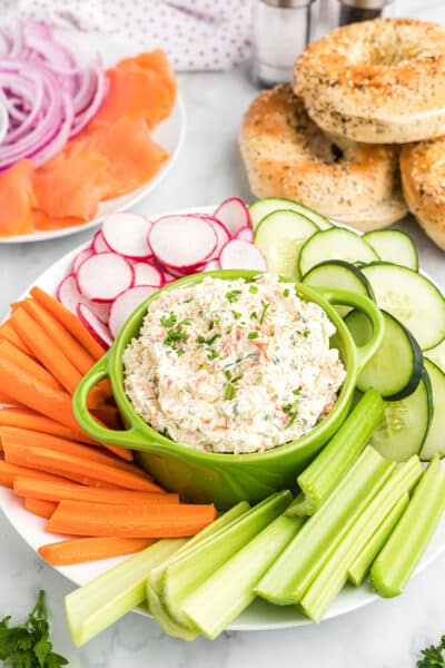a bowl of veggie cream cheese on a plate with sliced vegetables.