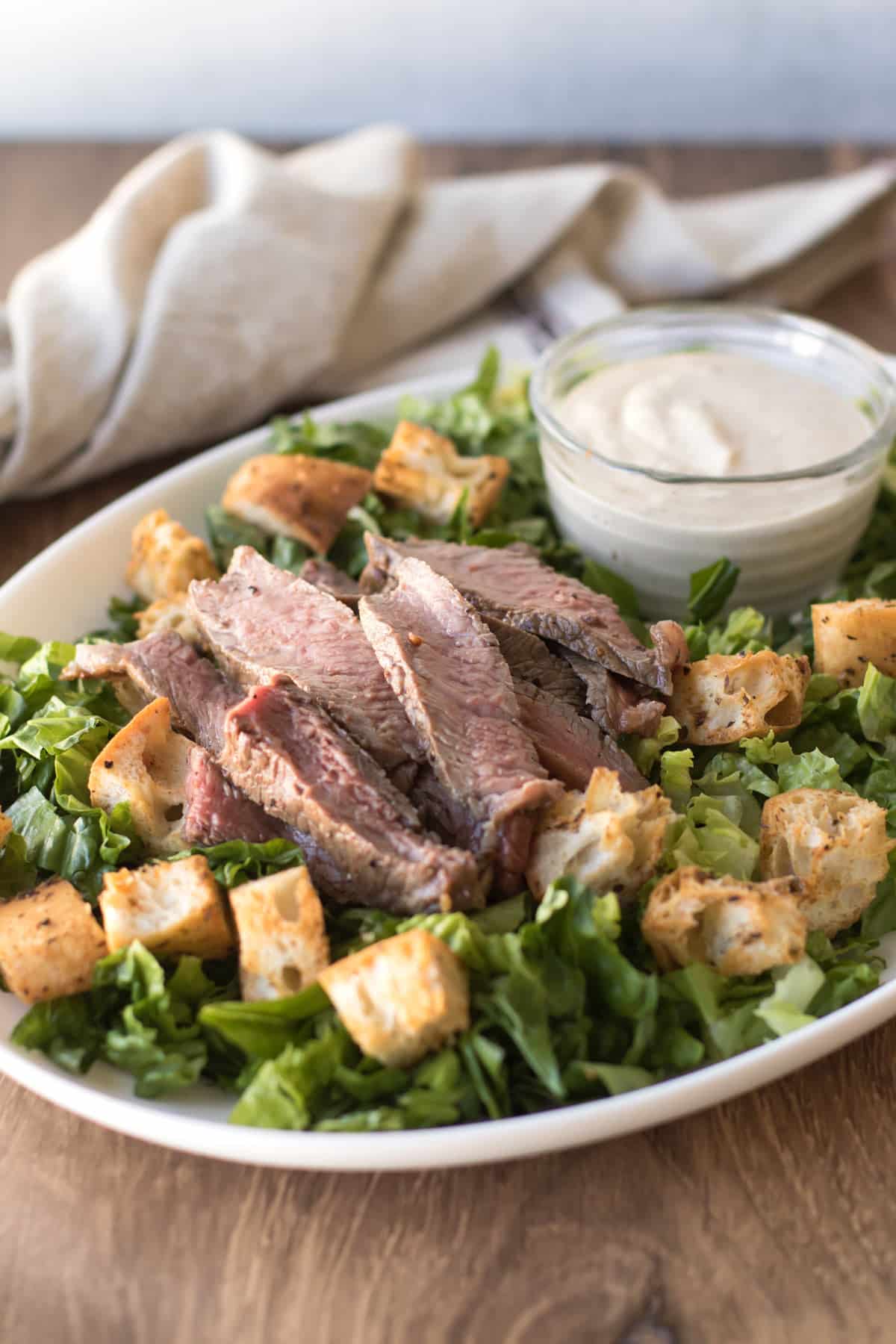 romaine lettuce topped with ciabatta croutons, steak, with a bowl of dressing.
