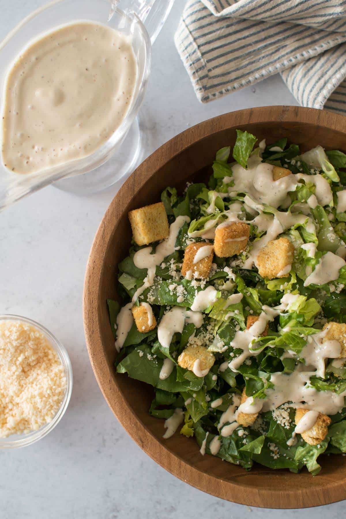 a caesar salad with a bowl of cheese and dressing on the side.