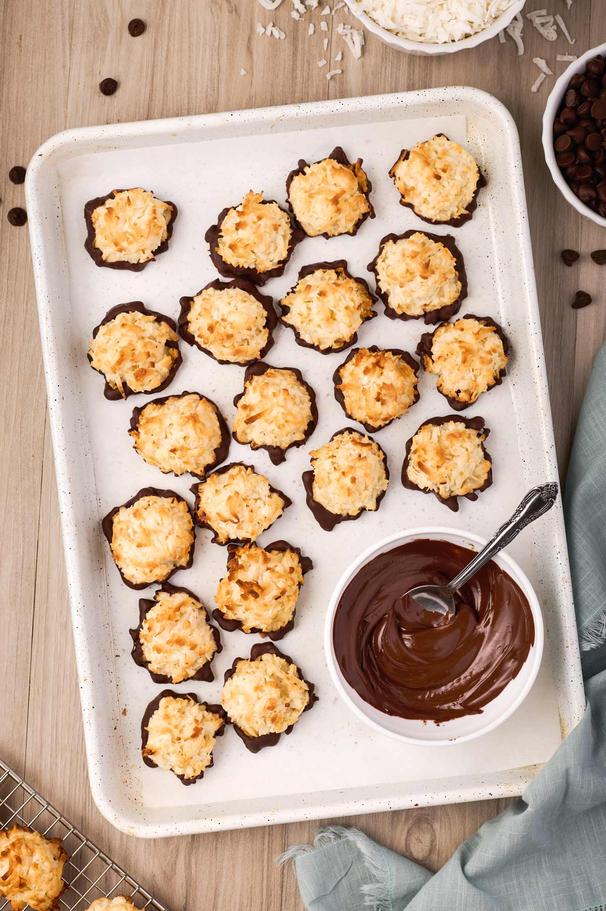 chocolate macaroons on a sheet pan with a bowl of melted chocolate.