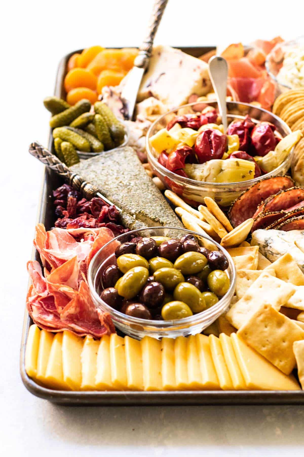 a cheeseboard with olives, sliced cheese, cheese wedges, crackers, and sliced meat.