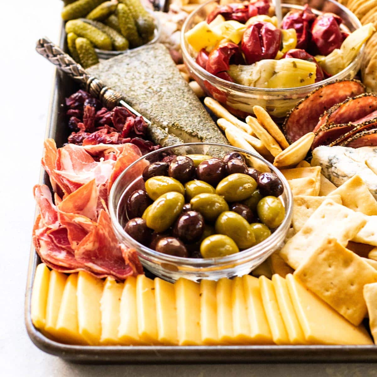 a cheeseboard with different types of cheese, crackers, cured meat, and olives.