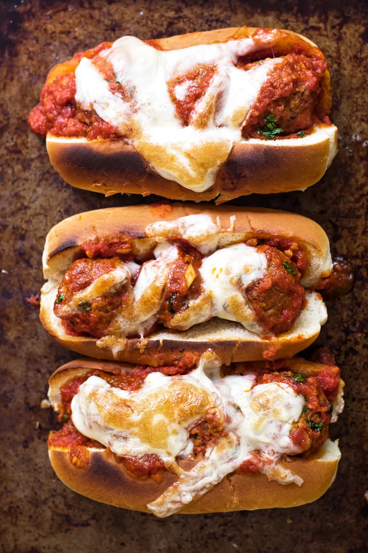 three meatball subs topped with melted cheese.
