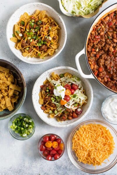 frito pie with bowls of toppings surrounding it.