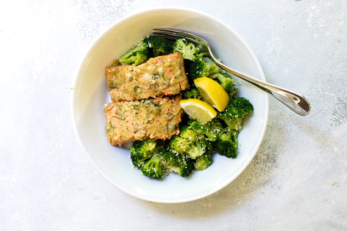 two pieces of salmon in a bowl with broccoli and lemon wedges.