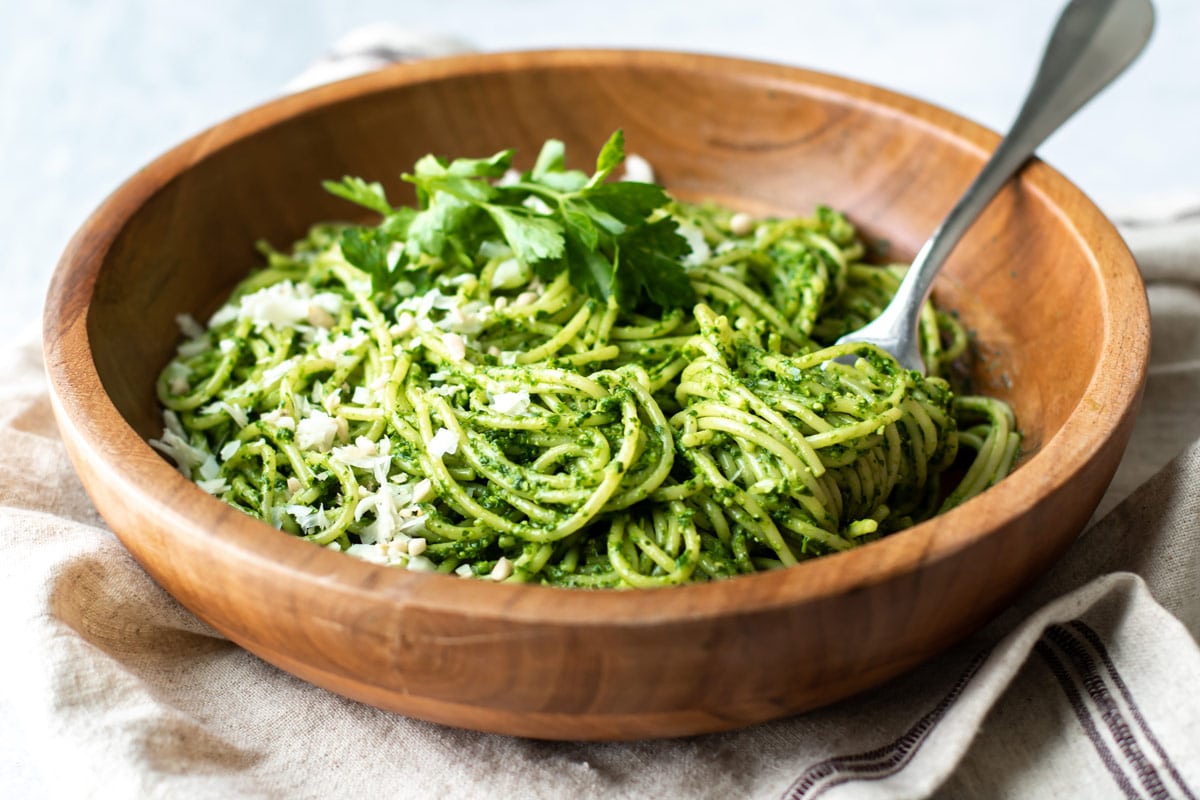 a bowl of pasta tossed with parsley pesto and garnished with cheese.
