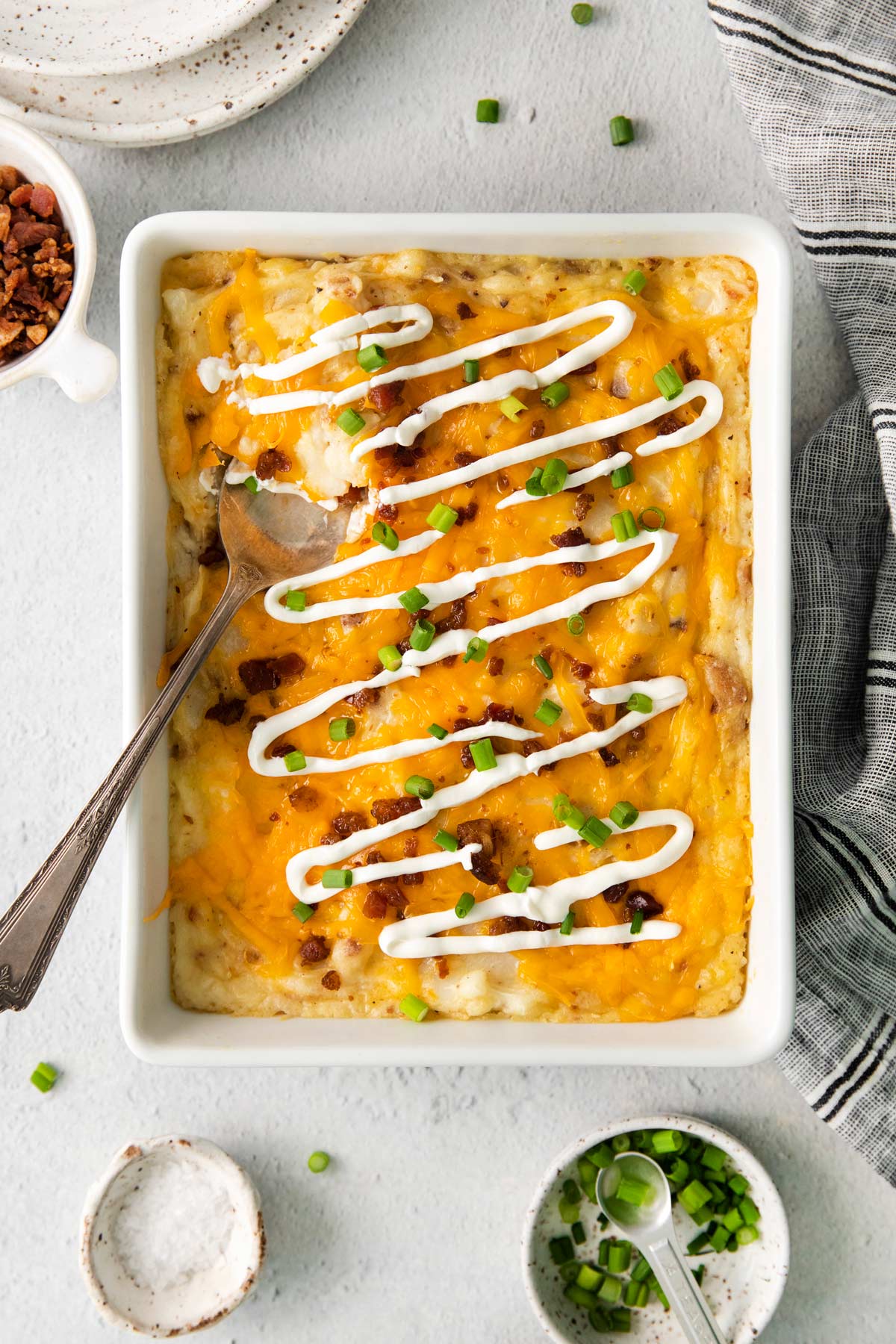 cheesy potato casserole in a baking pan with a spoon.