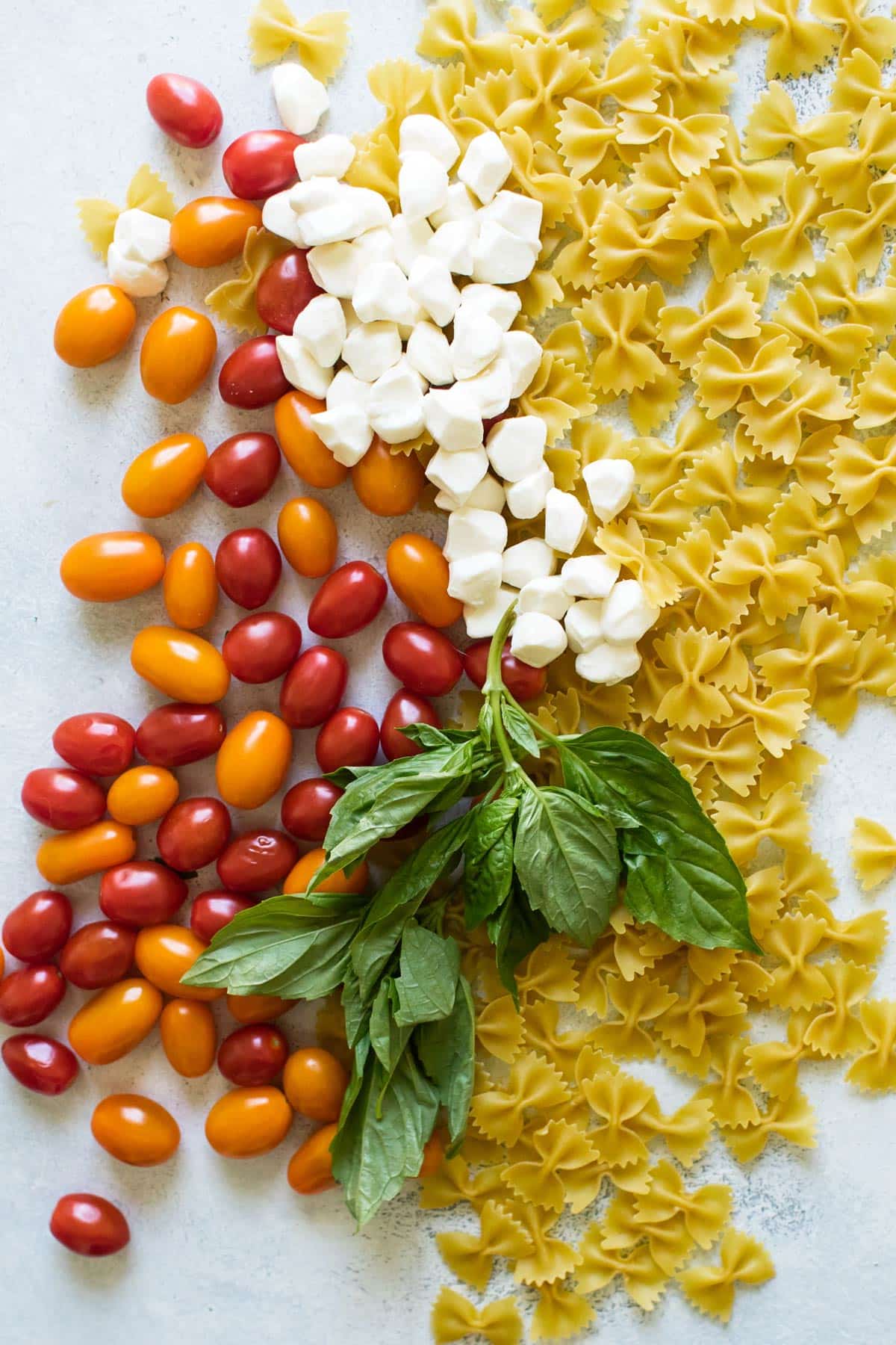 grape tomatoes, pasta, fresh basil leaves, and mozzarella balls spread out on a surface.