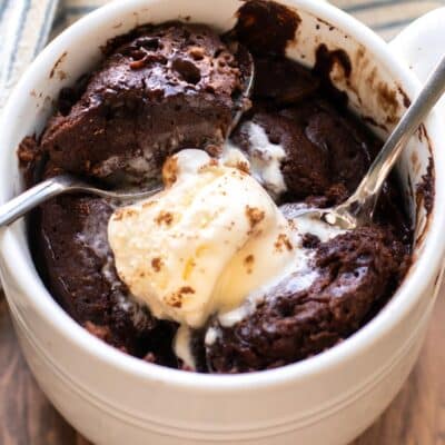 a chocolate mug cake topped with ice cream with two spoons.