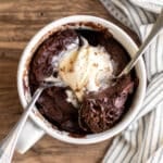 an overhead shot of the mug cake topped with ice cream with two spoons.