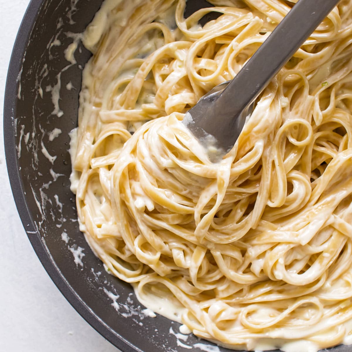 garlic pasta in a pan with tongs.