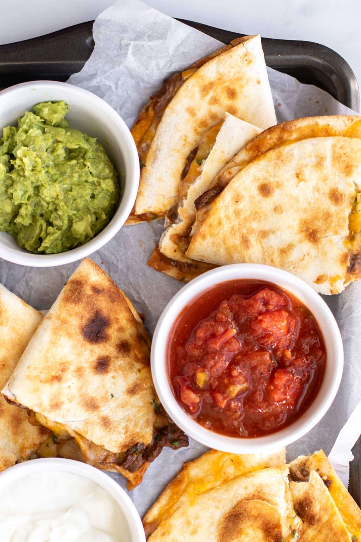 steak quesadillas with bowls of guacamole and salsa.