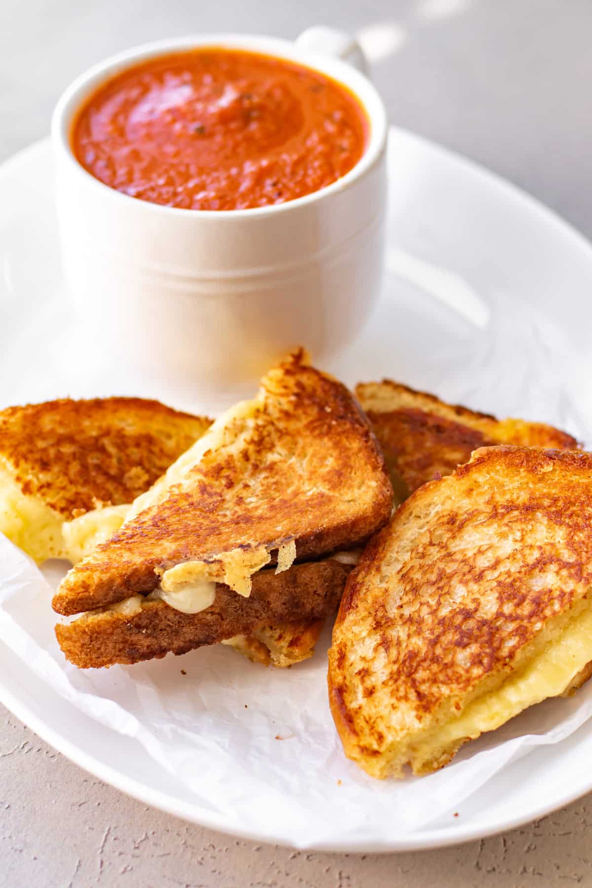 grilled cheese sandwiches on a plate with a mug of tomato soup.