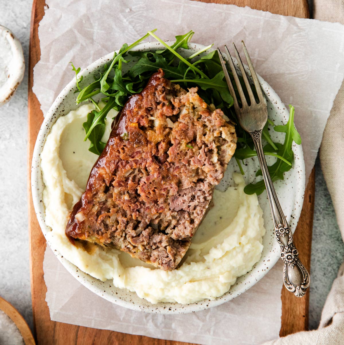 a sliced of BBQ glazed meatloaf on a plate with mashed potatoes and greens.