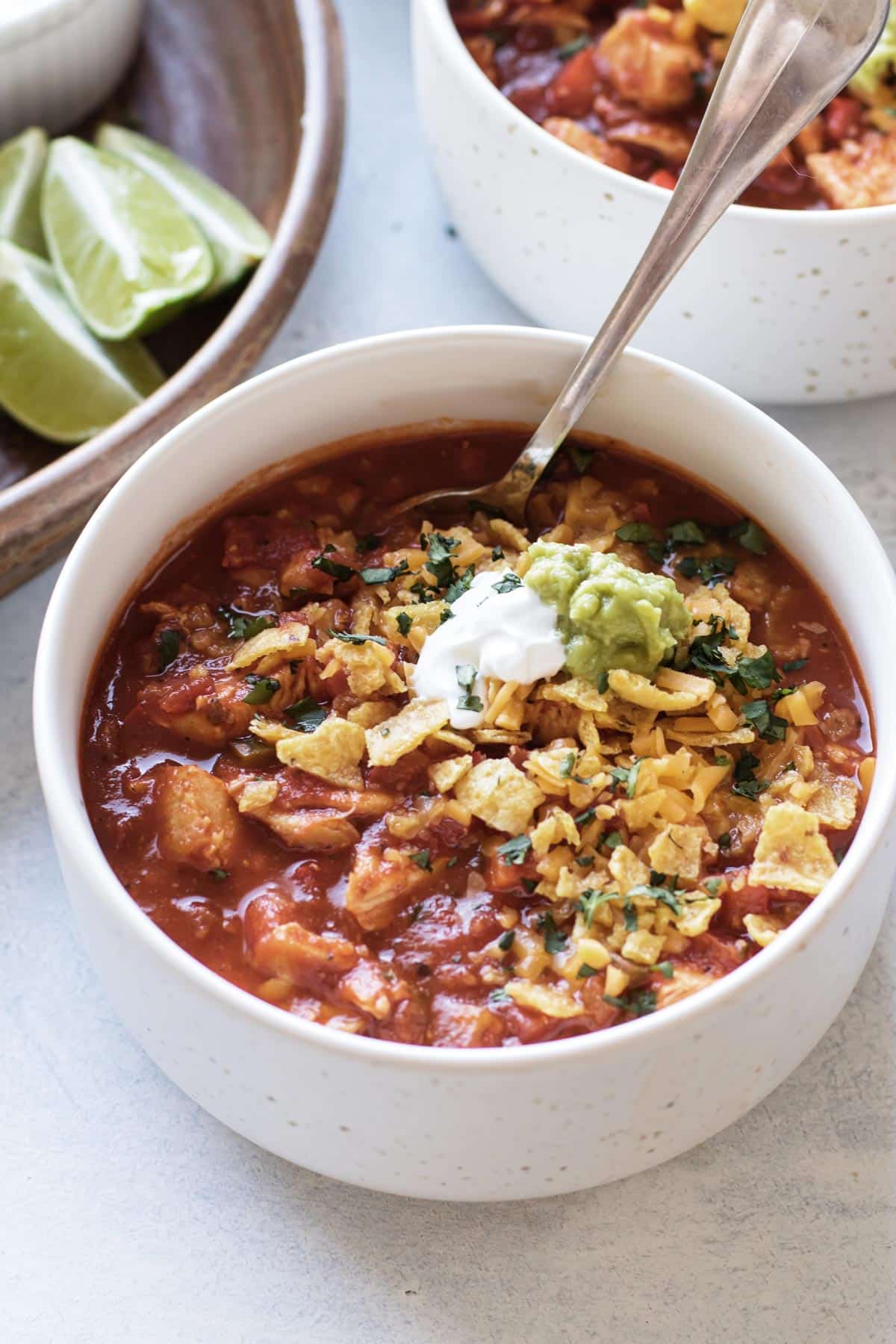a bowl of red chicken chili topped with fritos, sour cream, and guacamole.