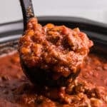 a ladle of Sunday sauce being lifted out of the slow cooker.