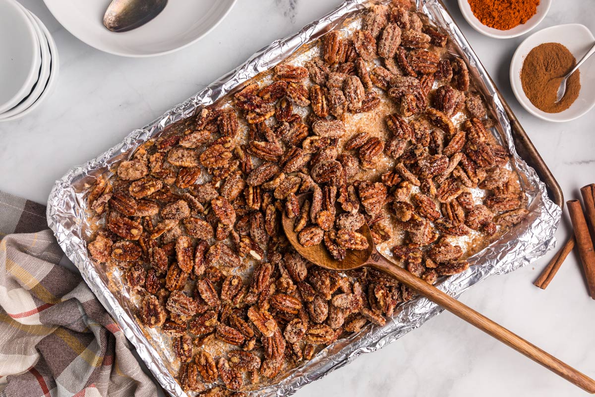 sweet and spicy pecans on a sheet pan with a wooden spoon.
