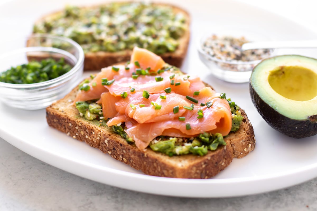 a slice of smoked salmon avocado toast on a plate with the other ingredients.