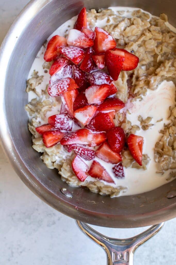strawberries and cream added to the cooked oatmeal in a pan.