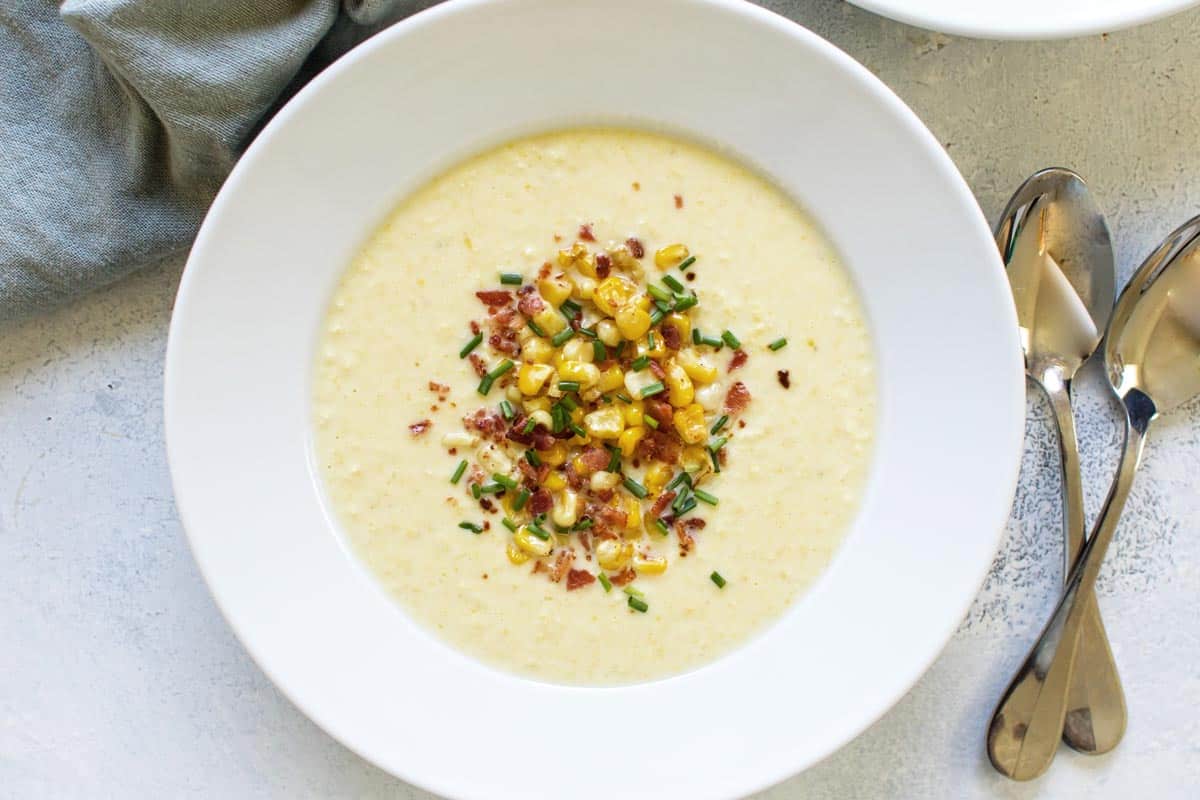 a bowl of fresh corn soup topped with bacon and corn.
