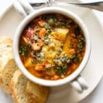 minestrone soup in a bowl on a plate with bread.