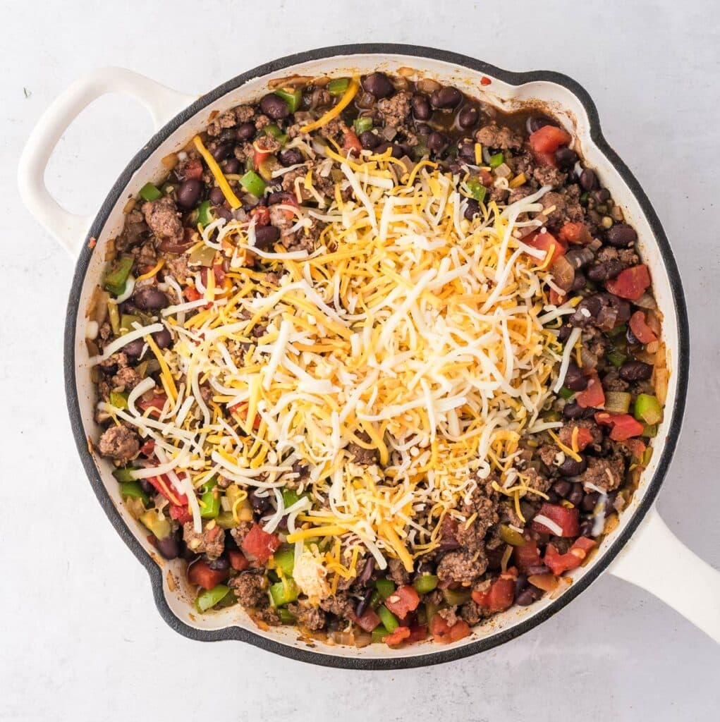 shredded cheese added on top of the other ingredients in the skillet.