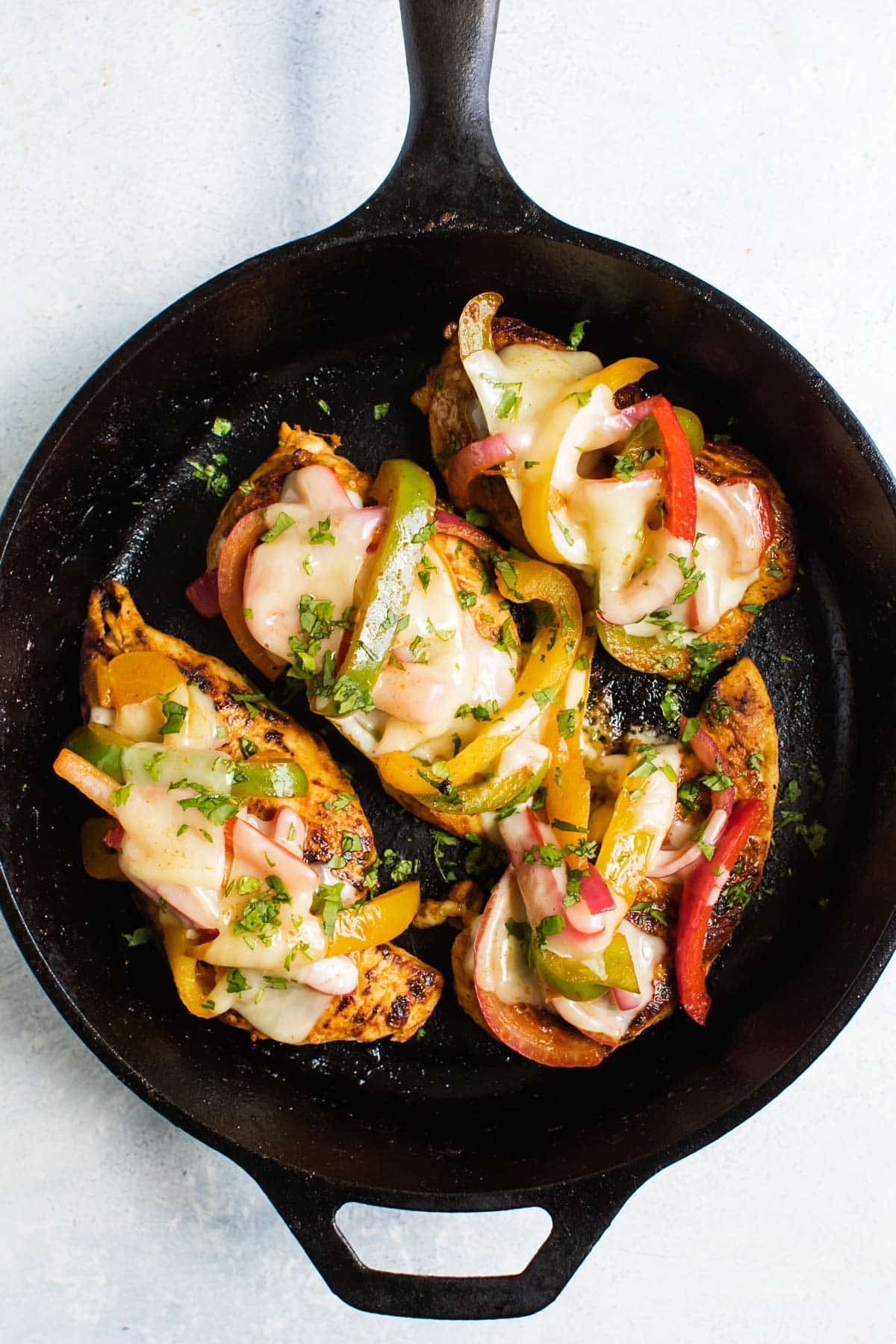 the chicken topped with cheese and peppers in a pan.