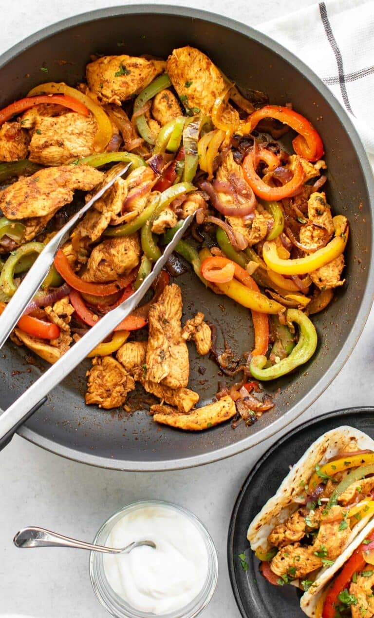 a pan of fajitas with tongs.
