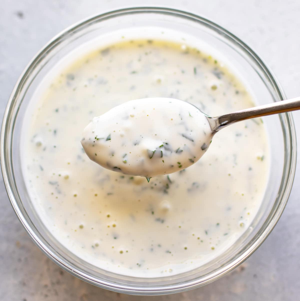 a bowl of dressing with a spoonful being held above the bowl.