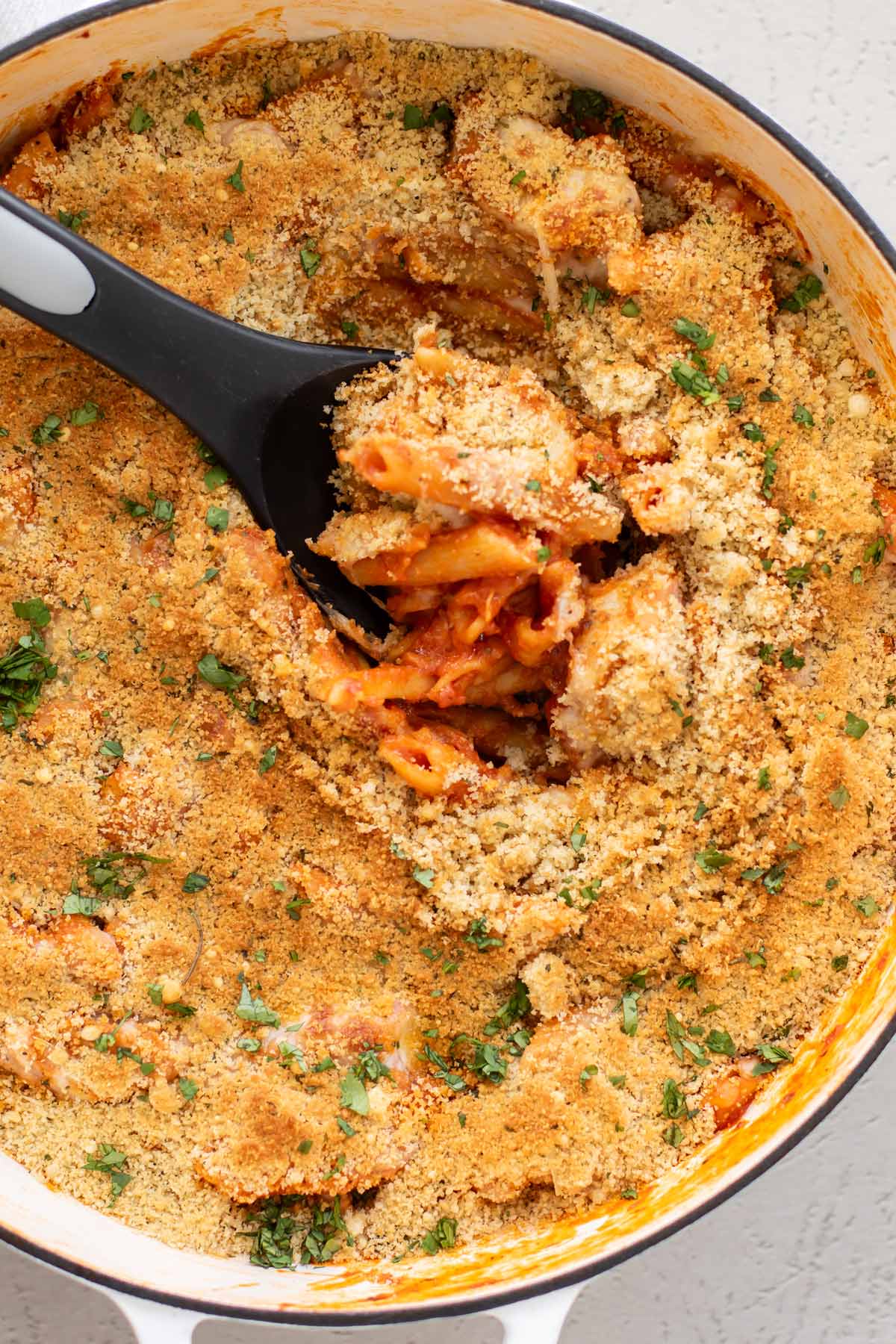 a serving spoon scooping out some chicken parm pasta from the pan.
