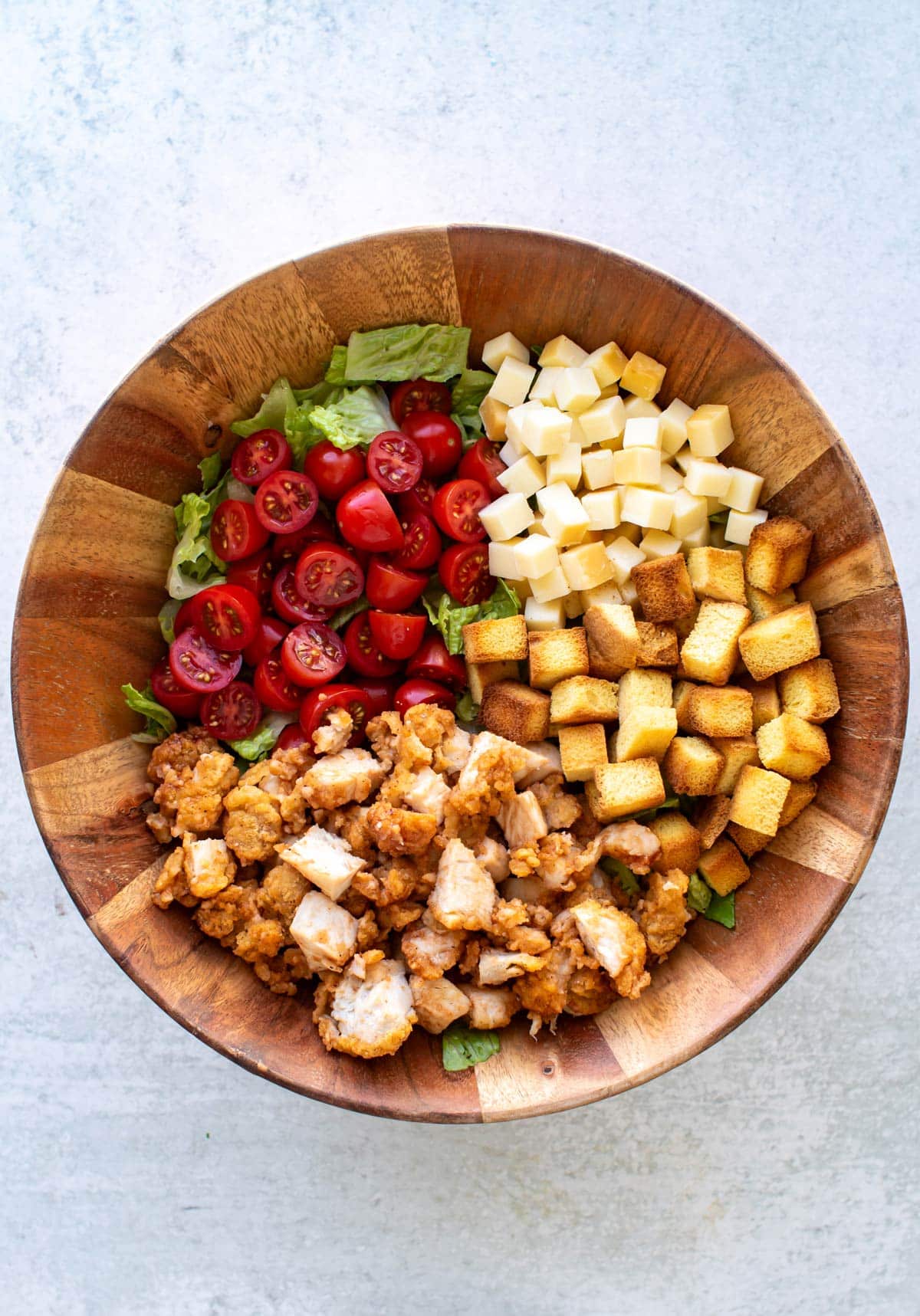 the tomatoes, croutons, cheese, and chicken on lettuce in a serving bowl.
