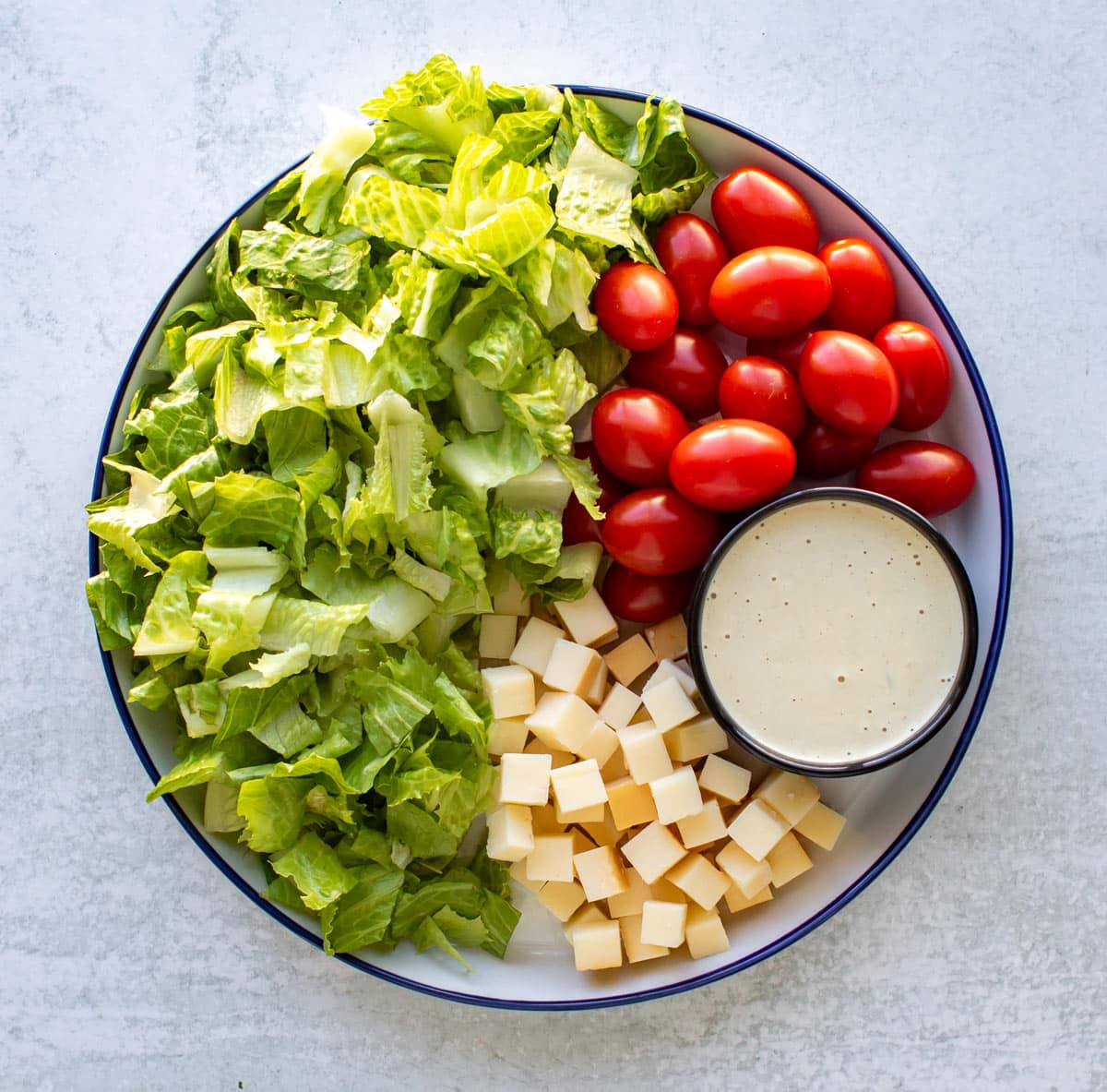 the lettuce, tomatoes, cheese, and a small bowl of dressing on a plate.