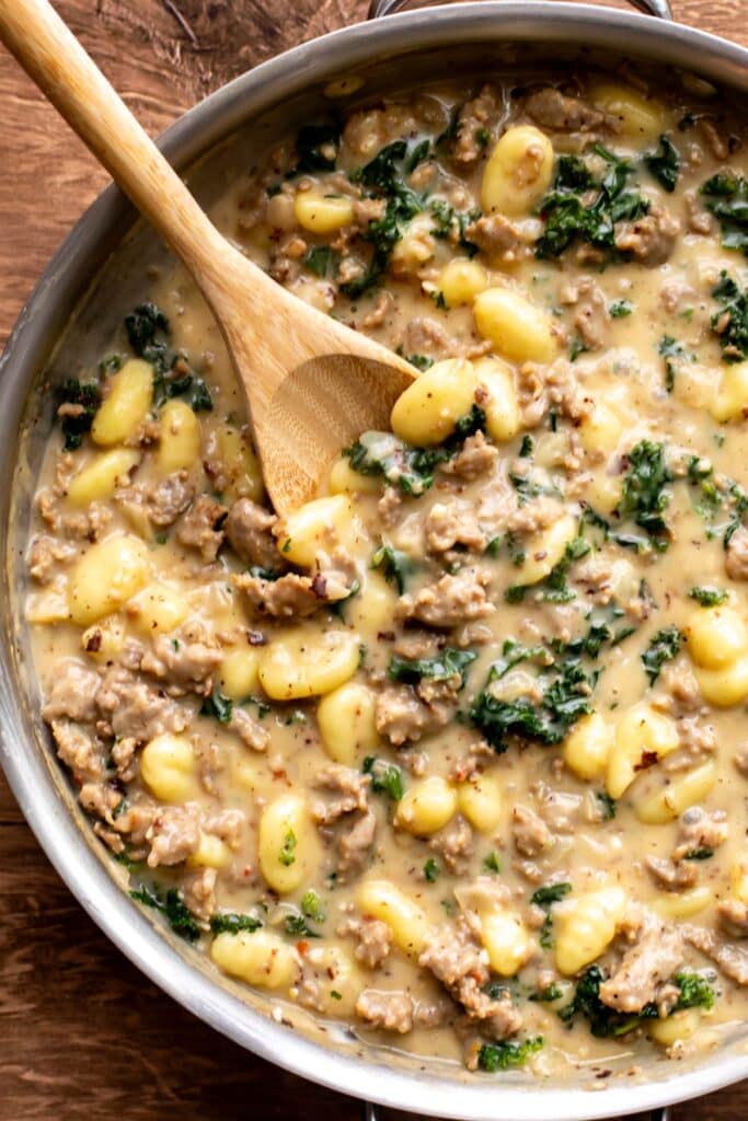 a pan of sausage gnocchi with kale being stirred.