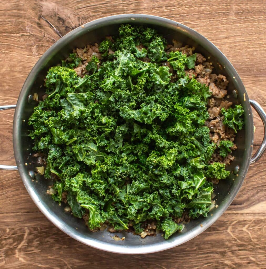fresh kale added to the pan with the sausage.
