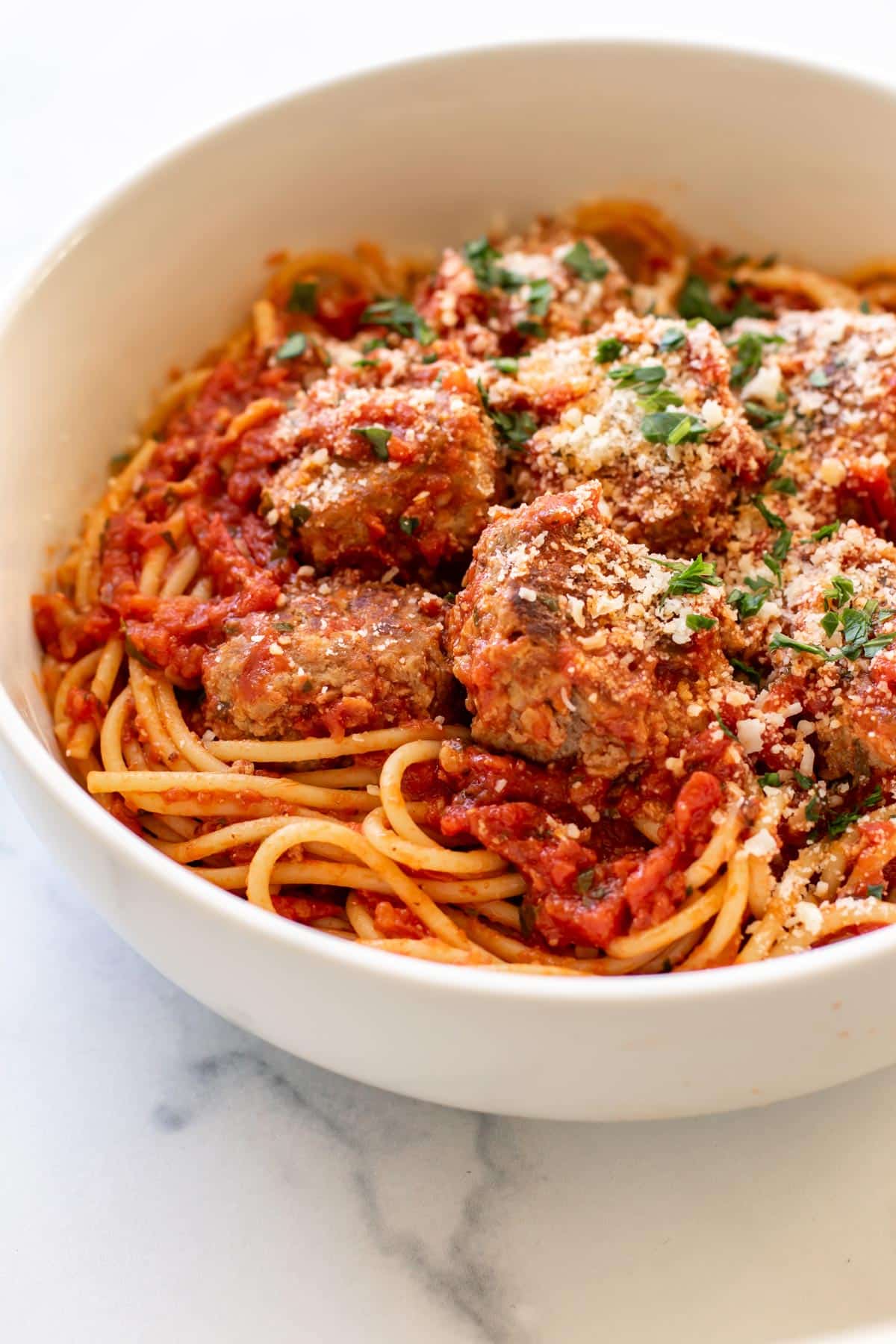 a bowl of spaghetti and meatballs garnished with parmesan cheese