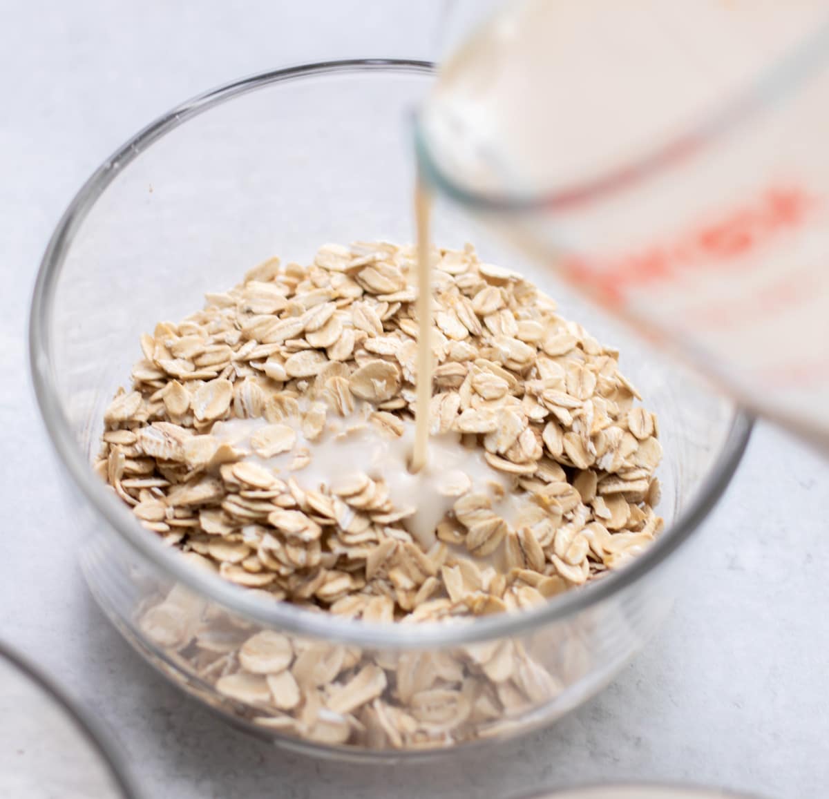 the milk and yogurt mixture being poured over oats in a container.